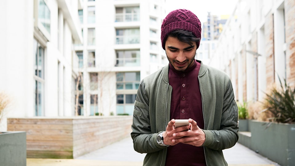 Man on street looking at mobile phone Make a delivery change to a UPS package by smart phone