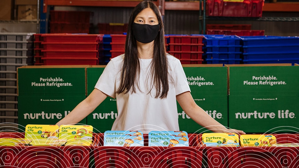 Woman wearing mask in tile 1 Jennier Chow in a mask sitting at a Nurture Life table